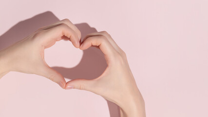 Young woman making heart with her hands on pink background, closeup