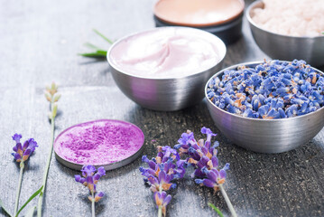 Fototapeta na wymiar beauty product samples with fresh purple and blue dried lavenders, bath salts and massage pouches on dark wood table background
