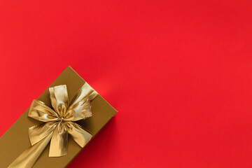 Golden gift box with golden ribbon and bow on a red background. Top view. Copy space.