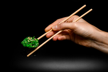 hand holds roll of gunkan sushi with chukka and sesame seeds wrapped in nori seaweed with...