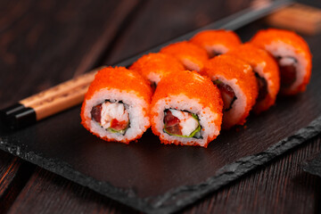 Sushi roll with shrimp and red pepper and tobiko caviar with salad served on black board close-up - Japanese food