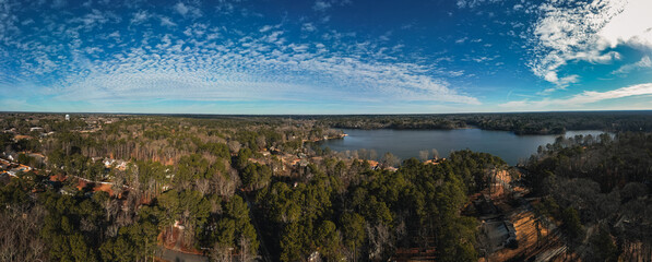 Aerial panoramic view of a beautiful lake in the middle of the forest and city houses, photography with drone.