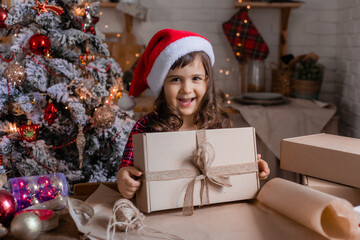 Fototapeta na wymiar a happy little girl at home in the kitchen is packing Christmas presents in crab boxes. new year's sale