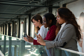 Three attractive businesswomen enjoy their break using their smartphones. Copy space on the left.