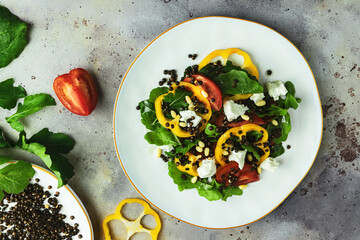 Top view of fresh vegetable salad with black lentil, cheese, yellow bulgarian pepper, arugula and pine nuts on white ceramic plate on rustic gray background. Top view. Close-up. Flat lay composition.