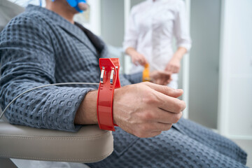 Fototapeta na wymiar Man in hospital gown sits with sensors on his wrists