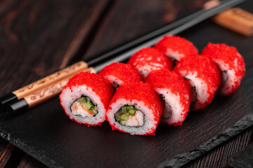 Sushi roll with shrimp and cucumber and tobiko caviar served on black board close-up - Japanese food