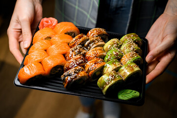 set of Philadelphia and Green dragon sushi rolls on tray in male hands
