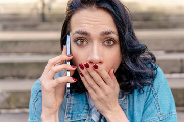 Outdoor portrait of an upset young woman in a denim jacket is talking on the phone  Lifestyle photo