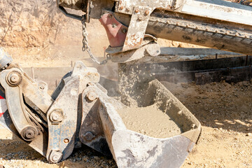 Concrete mixer truck pouring fresh wet concrete into excavators bucket at a construction site
