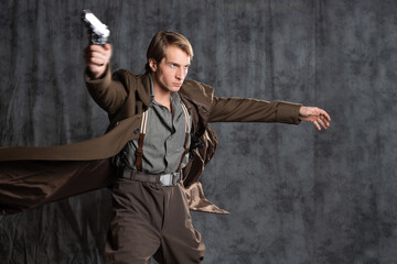hero in a military style with a gun in his hands, a young man in a long brown coat and breeches with suspenders. he shoots a pistol in a spectacular pose, his coat flutters behind his back