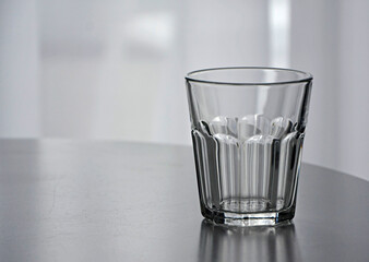 pusta szklanka na stole, empty glass, empty glass on the table in an empty room - obrazy, fototapety, plakaty