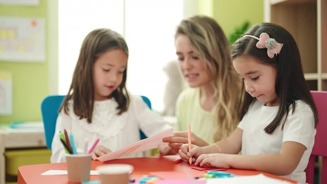 Teacher with girls sitting on table having handcrafts class at kindergarten