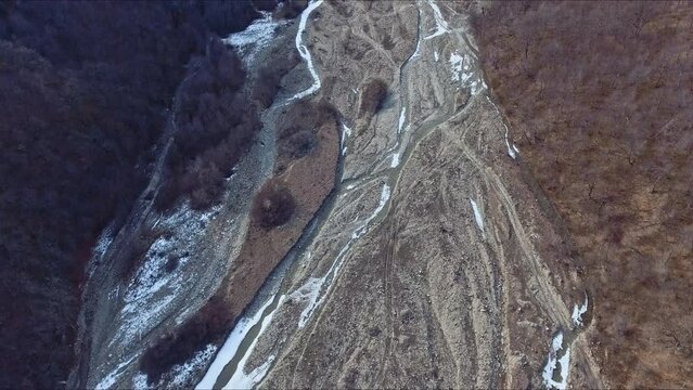 Dried up river bed in a rural countryside with the snowy mountains in the background. Majestic landscape with the rock road and hills.