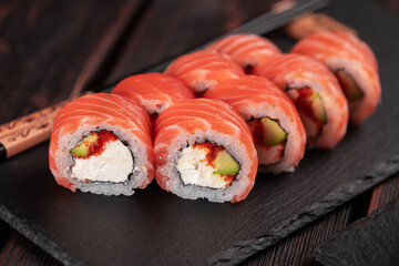 Sushi roll maguro with salmon avocado and tobiko, philadelphia cheese on black board close-up. Sushi menu. Japanese food.