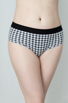 Close up photo of a woman's body. She is wearing black plaid underwear. Panties product shot. The woman is caucasian and has pale skin. 
