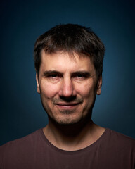 Portrait of a 42-year-old brunette man on a dark background with bright illumination