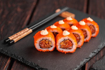 Sushi roll with tuna, onion in batter and tobiko caviar served on black board close-up - Japanese food