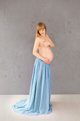 A naked pregnant woman covers her breasts. long blue skirt