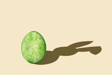 Green easter egg with bunny shadow on yellow surface