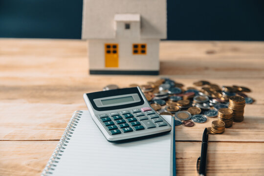 Calculator, coins, house and notepad on the table