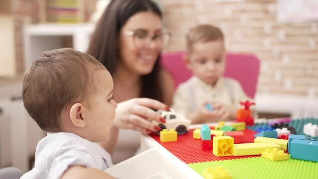 Teacher with boys playing with construction blocks sitting on table at kindergarten