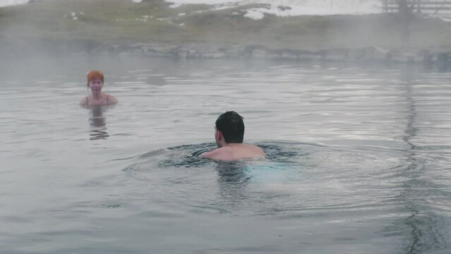 Hot spring geothermal spa on Iceland. Romantic couple in love relaxing in hot pool on Iceland. Young woman and man enjoying bathing relaxed in a blue water lagoon Icelandic tourist attraction. Sunset