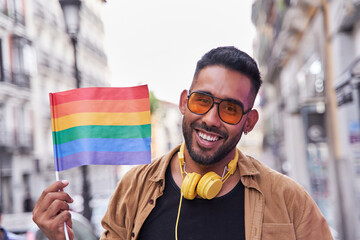 hiispanic man with beard and sunglasses raises a lgtbi flag.