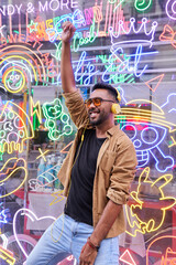 Obraz na płótnie Canvas Hispanic male listening to music with headphones. young man with beard, sunglasses and casual clothes dancing with neon lights background.