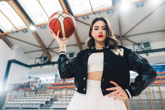 Bottom view of brunette cheerleader holding a basketball in her hand. The ceiling and stands blurred in the background. High quality photo