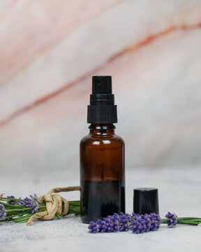 water or face toner in amber glass spray bottle on marble white and pink background with fresh lavender flowers.     