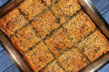 Greek traditional homemade Spinach Pie already baked and cutted in square portions in a large stainless steel baking pan ontop of a blue wooden table