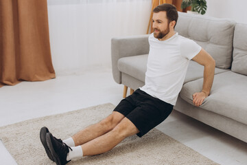 Positive athletic bearded middle-aged man stretching at home, using laptop, watching sport videos on Internet, having fitness class online, copy space. Healthy lifestyle, sport on self-isolation