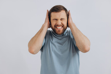 Portrait of a modern bearded middle-aged man in a blue t-shirt showing emotions covering his ears on a white background