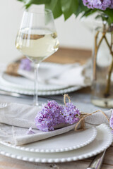 Beautiful table decor for a wedding dinner with a spring blooming lilac flowers. Celebration of a special event. Fancy white plates, wineglasses. Countryside style
