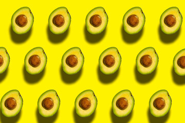Top view of a pattern of green avocados with a stone on a yellow background. Healthy summer food.