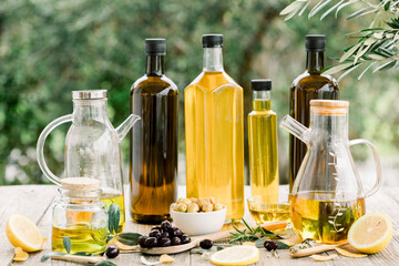 Olive oil bottle and olive oil in glass on old wooden table under olive tree.