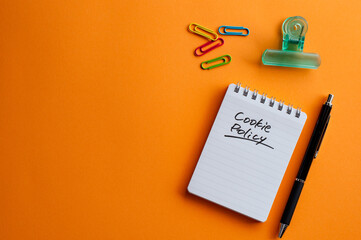 There is a notebook with the word Cookie Policy. It's placed on a color background.