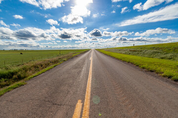 Empty rural road surrounded by cow pasture on sunny day with fluffy clouds in sky
