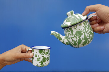 image of a hand pouring water from a teapot into a cup held by another person on blue isolated...