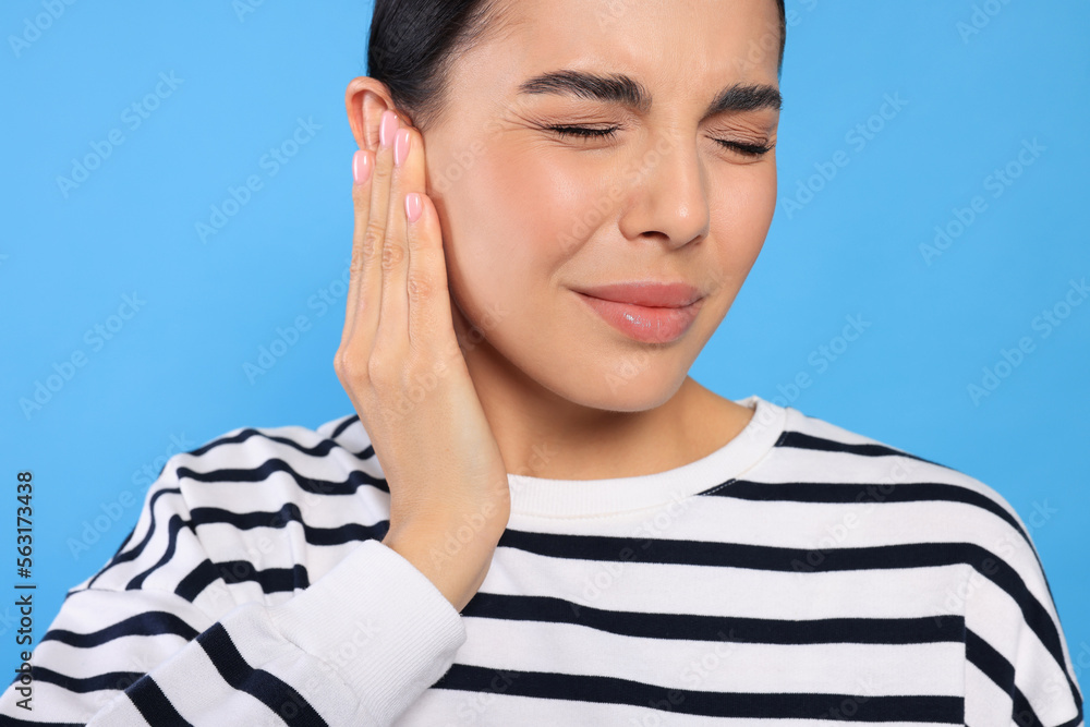 Poster Young woman suffering from ear pain on light blue background, closeup