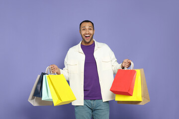 Happy African American man with shopping bags on purple background