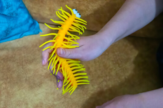 A closeup photo of a bright yellow rubber toy with rubbery hairs and legs, that resembles a caterpillar with a funny drawn on face, being held in a male hand