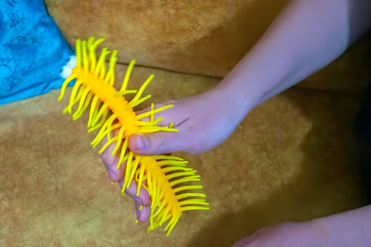 A closeup photo of a bright yellow rubber toy with rubbery hairs and legs, that resembles a caterpillar with a funny drawn on face, being held in a male hand