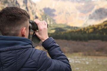 Boy looking through binoculars in beautiful mountains, back view. Space for text