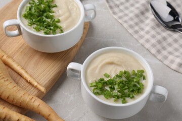 Bowls with tasty creamy soup of parsnip served on light grey table, closeup