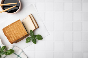 Delicious smoked tofu, soy sauce and basil on tiled table, flat lay. Space for text