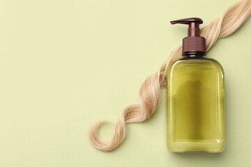 Lock of hair and shampoo bottle on olive background, flat lay. Space for text