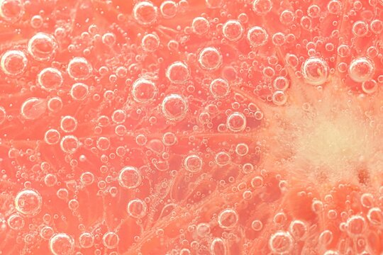 Slice of grapefruit in sparkling water. Grapefruit slice covered by bubbles in carbonated water. Grapefruit slice in water with bubbles