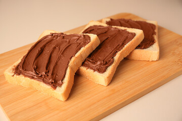 Tasty toasts with chocolate paste on beige background, closeup